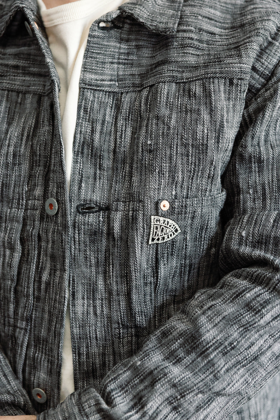 Close-up front view of male model wearing textured gray shirt with button details, chest pocket, and woven brand patch.