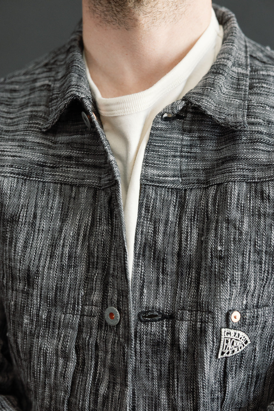 Close-up front view of male model wearing textured gray shirt with collar, buttons, and chest pocket detail.