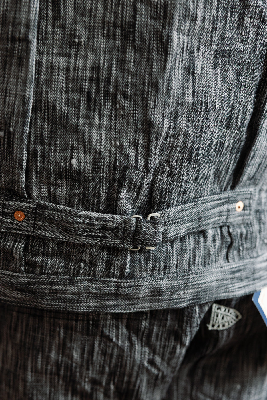 Close-up of dark selvedge denim shirt front, showing textured fabric, button details, and belt loop.