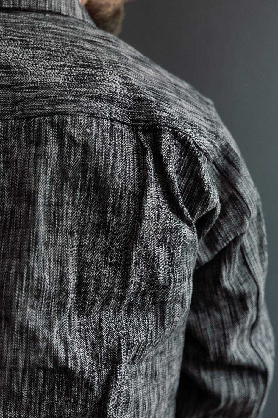 Close-up back view of male model in textured gray shirt, showcasing fabric detail and shoulder seam.