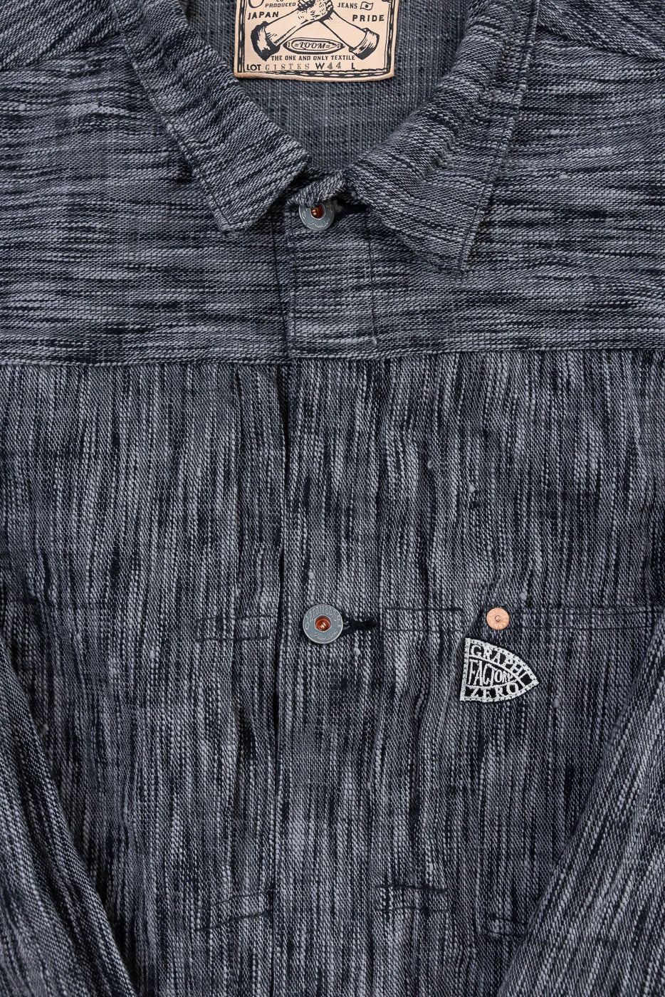 Close-up front view of men's selvedge shirt: textured fabric, button placket, collar tag, and chest pocket detail.