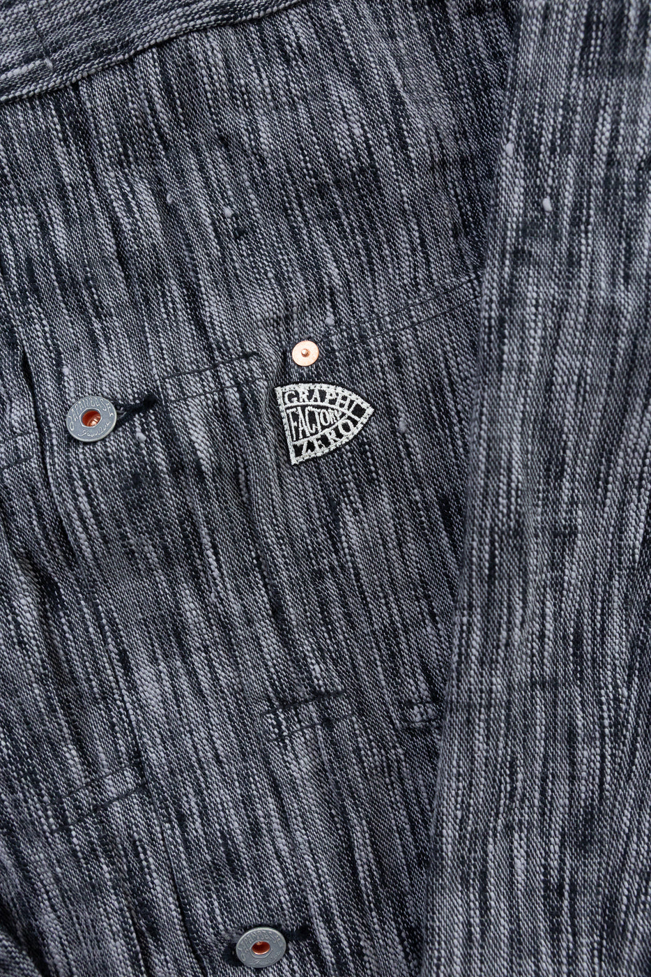 Close-up front view of dark denim shirt with 'Graphite Factory Zero' patch, copper buttons, and textured fabric.