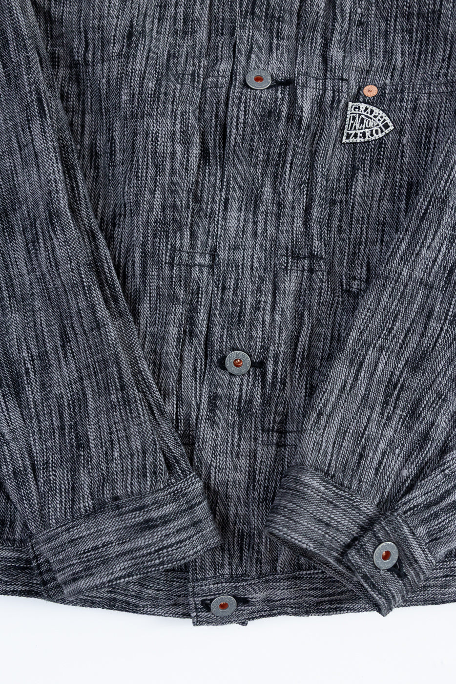 Close-up front view of dark gray textured shirt with button details, chest patch, and rolled sleeves