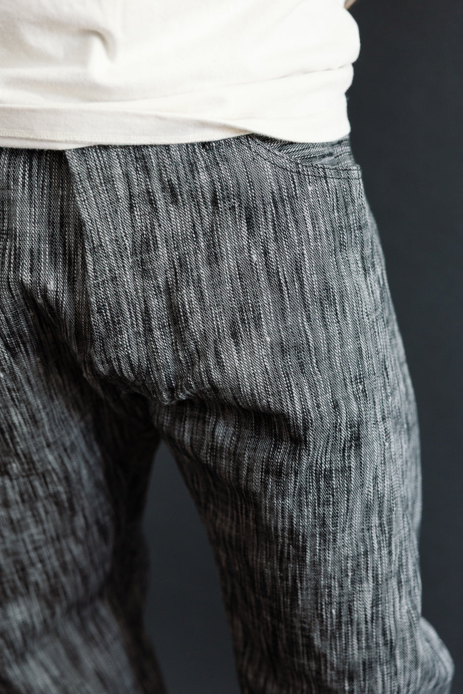 Close-up side view of men's textured selvedge pants, showing fabric weave and back pocket detail on athletic build model.