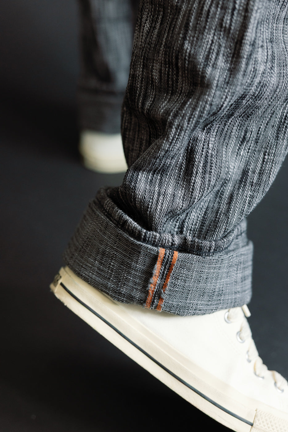 Close-up of male model's cuffed selvedge jeans with orange stitching, paired with white sneakers.