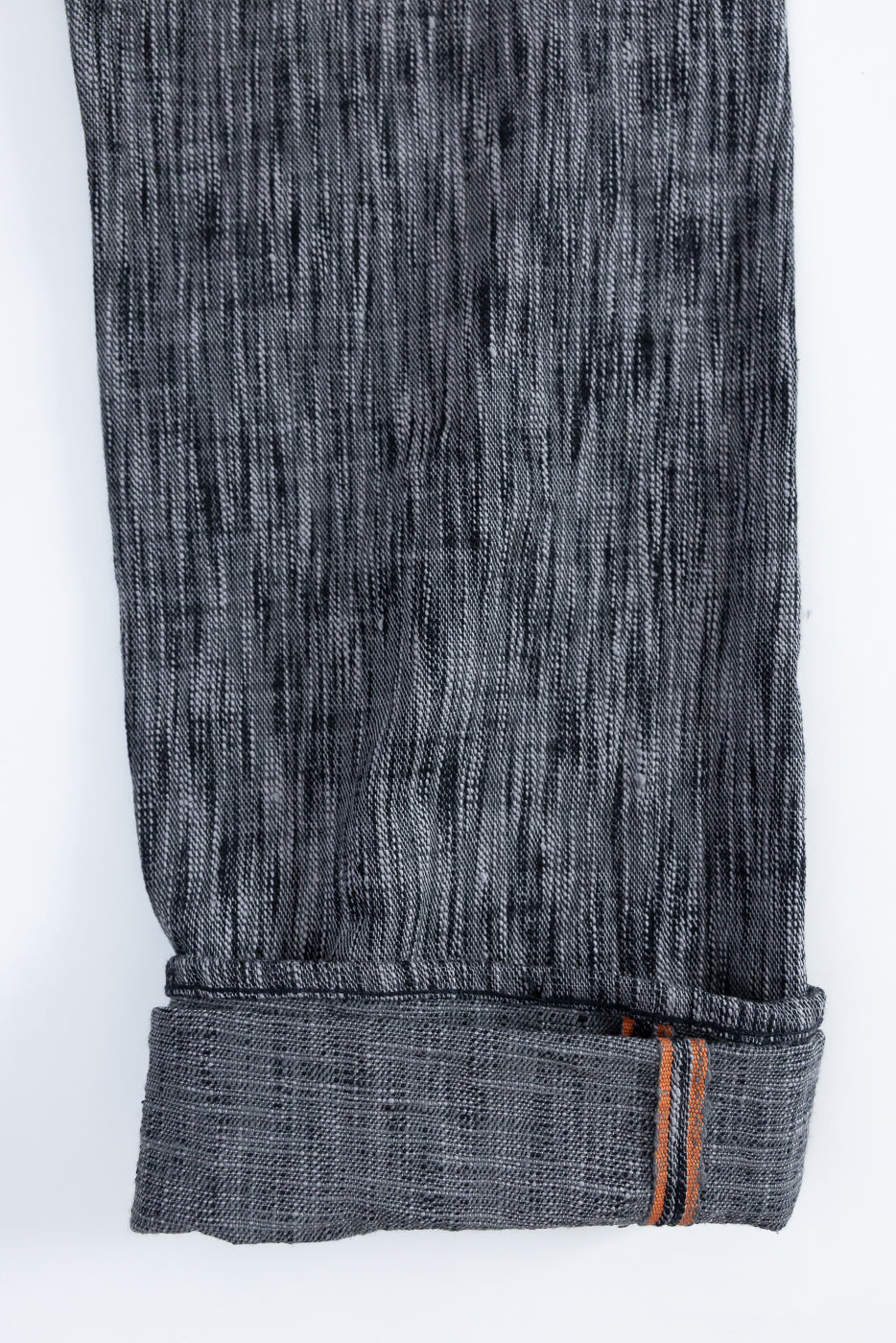 Close-up of selvedge denim pants hem, showcasing texture and orange stitching detail