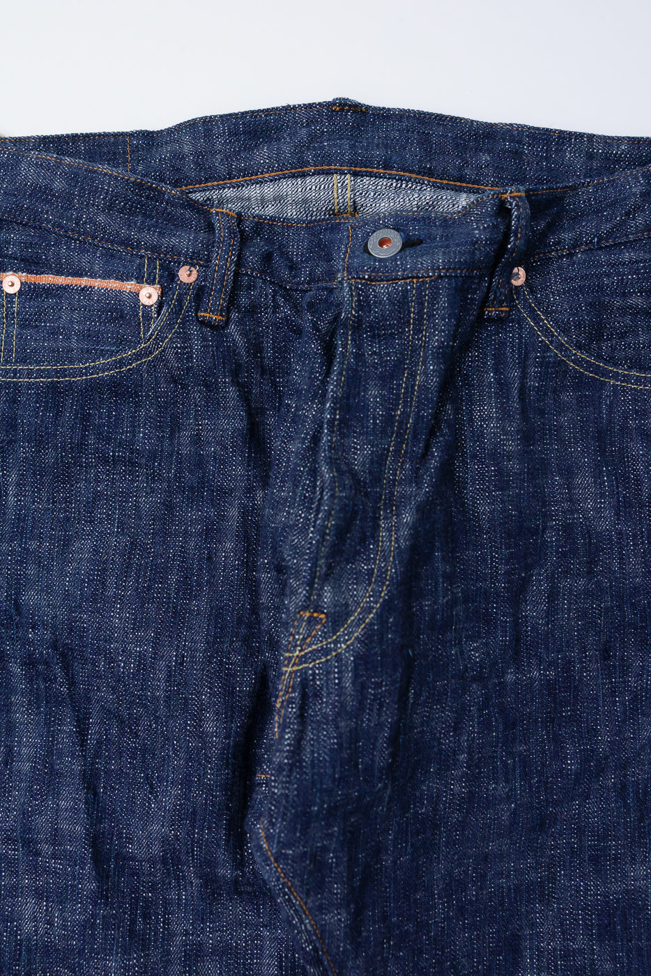 Close-up of 15oz Skein Dyed Slubby Green Indigo Selvedge Jeans - Slim Straight Fit, highlighting the waistband, unfastened fly, contrast stitching, coin pocket with copper rivets, and the textured raw denim fabric.