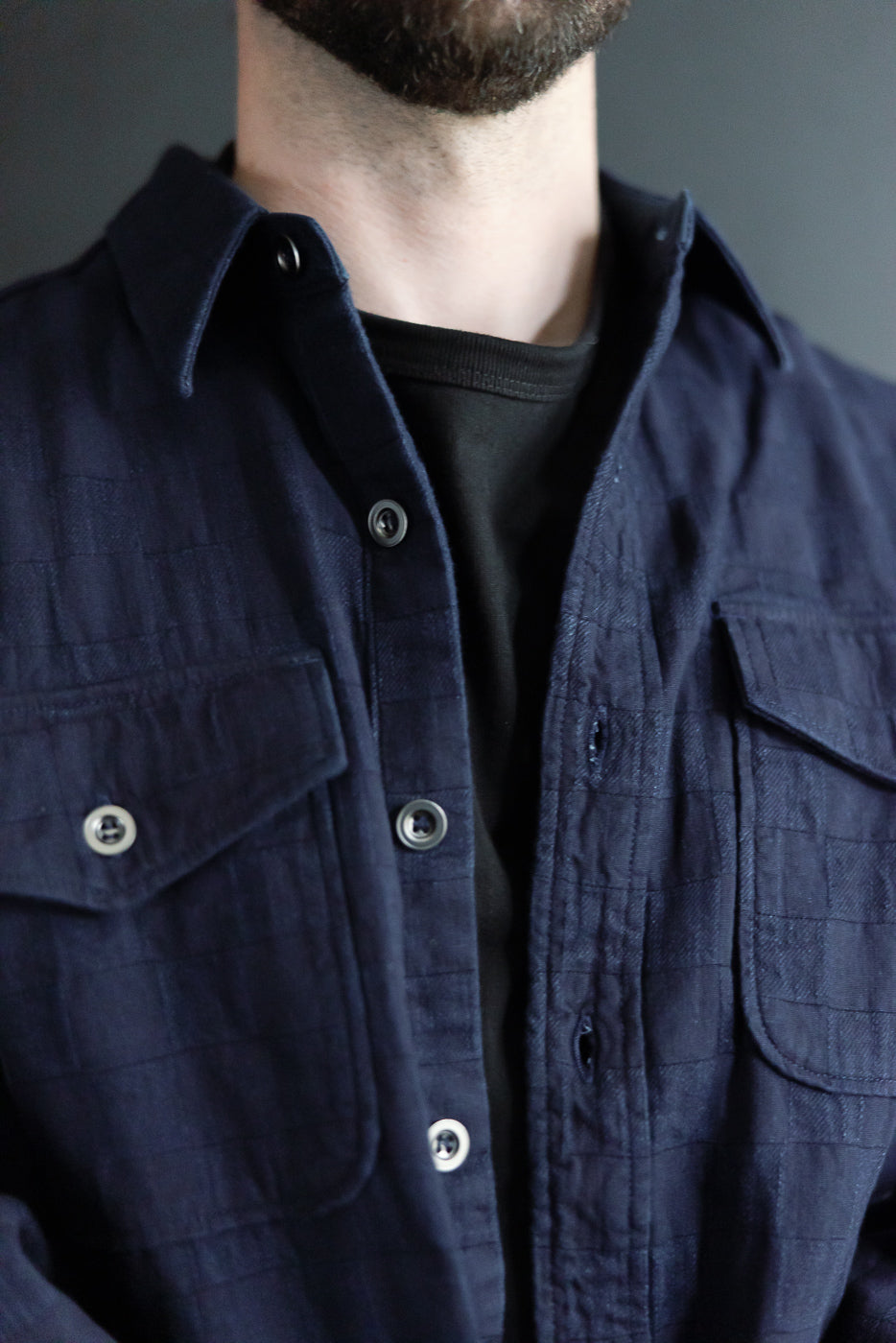 Close-up front view of navy shirt with buttons, collar, and chest pockets on male model