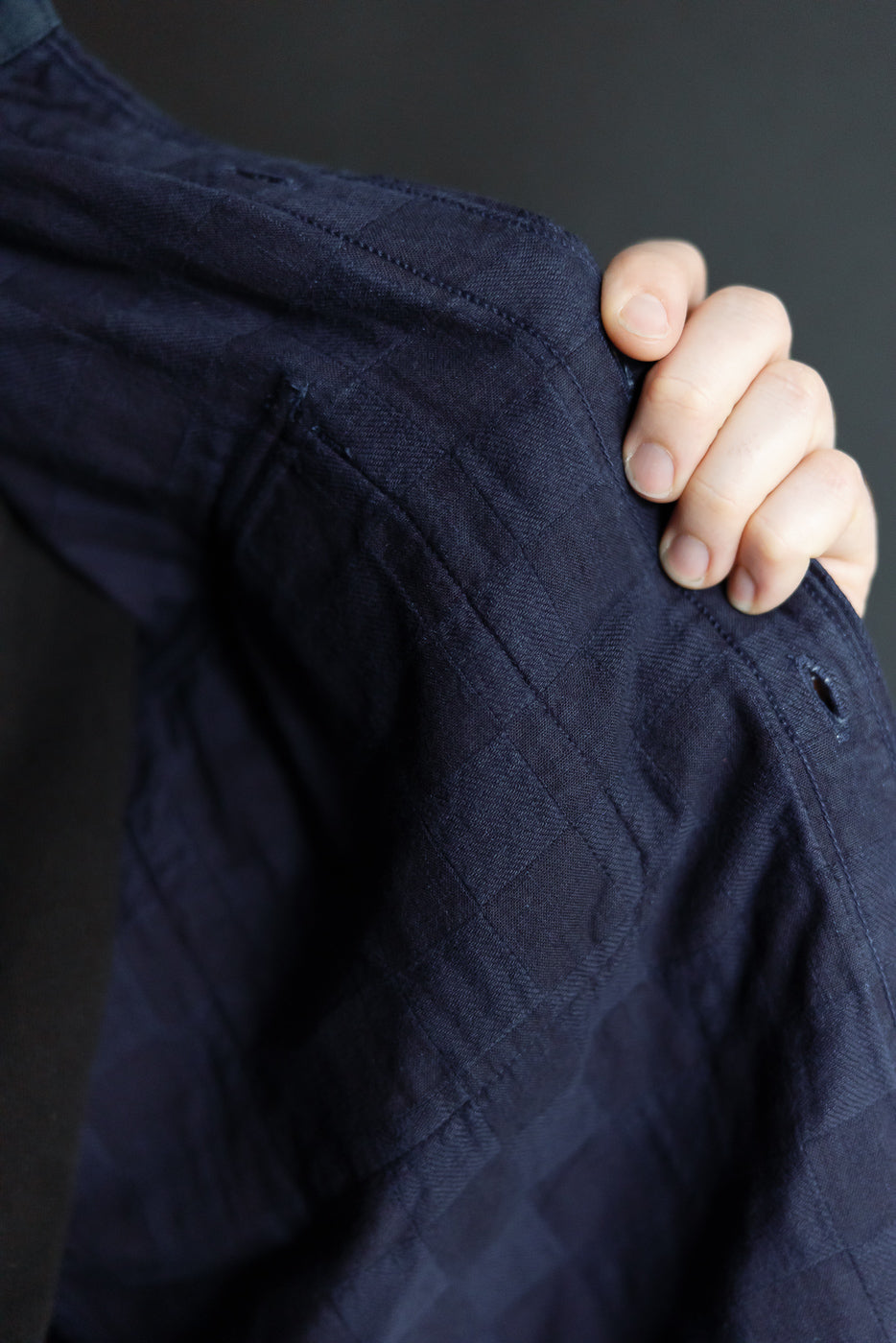 Close-up of navy quilted shirt shoulder, showing texture and stitching detail, worn by male model