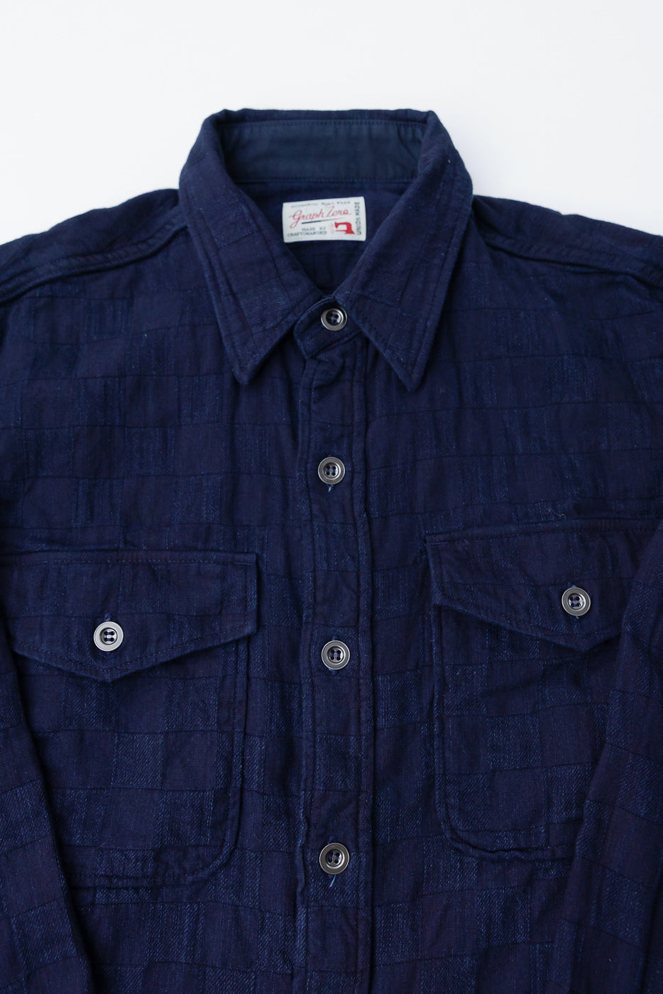 Close-up front of Graph Zero indigo jacquard plaid officer shirt, showing chest pockets, buttons, collar, and textured fabric at Dant.