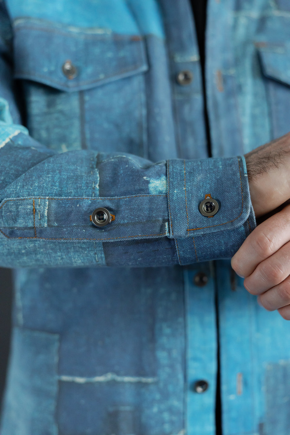 Close-up of male model's left sleeve cuff on patchwork denim shirt, showing button detail and selvedge texture.