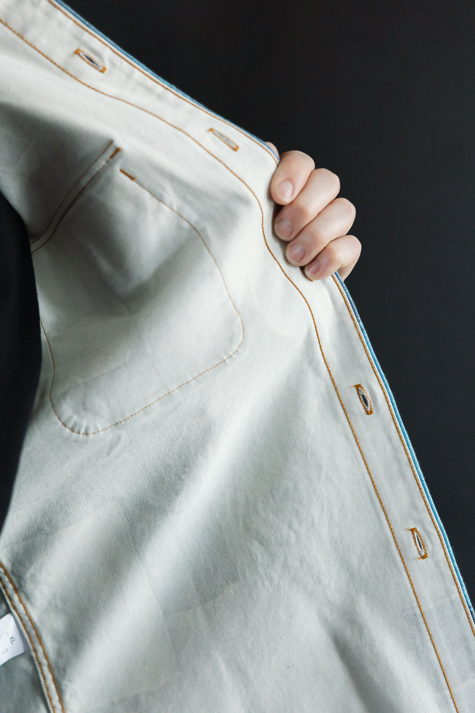 Close-up of light denim jacket front, showing orange stitching, chest pocket, and selvedge edge detail