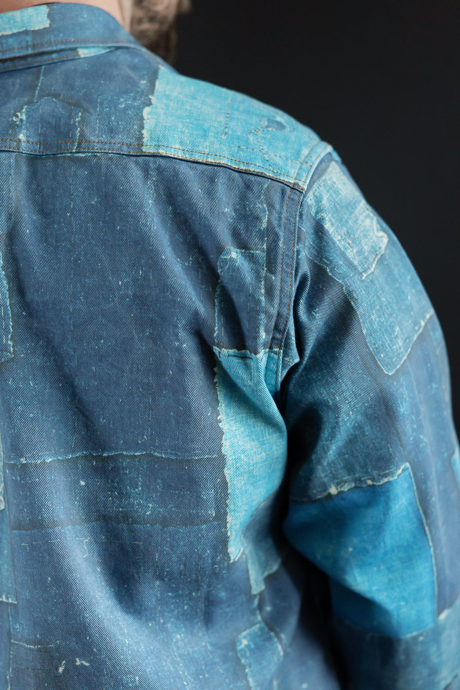 Close-up back view of male model's patched denim shirt, showcasing texture and stitching details.