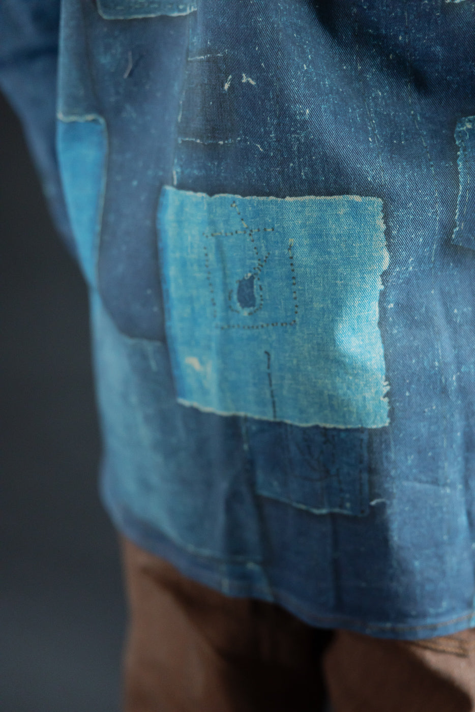 Close-up side view of indigo denim shirt with patchwork details, visible stitching, and fabric texture on male model.