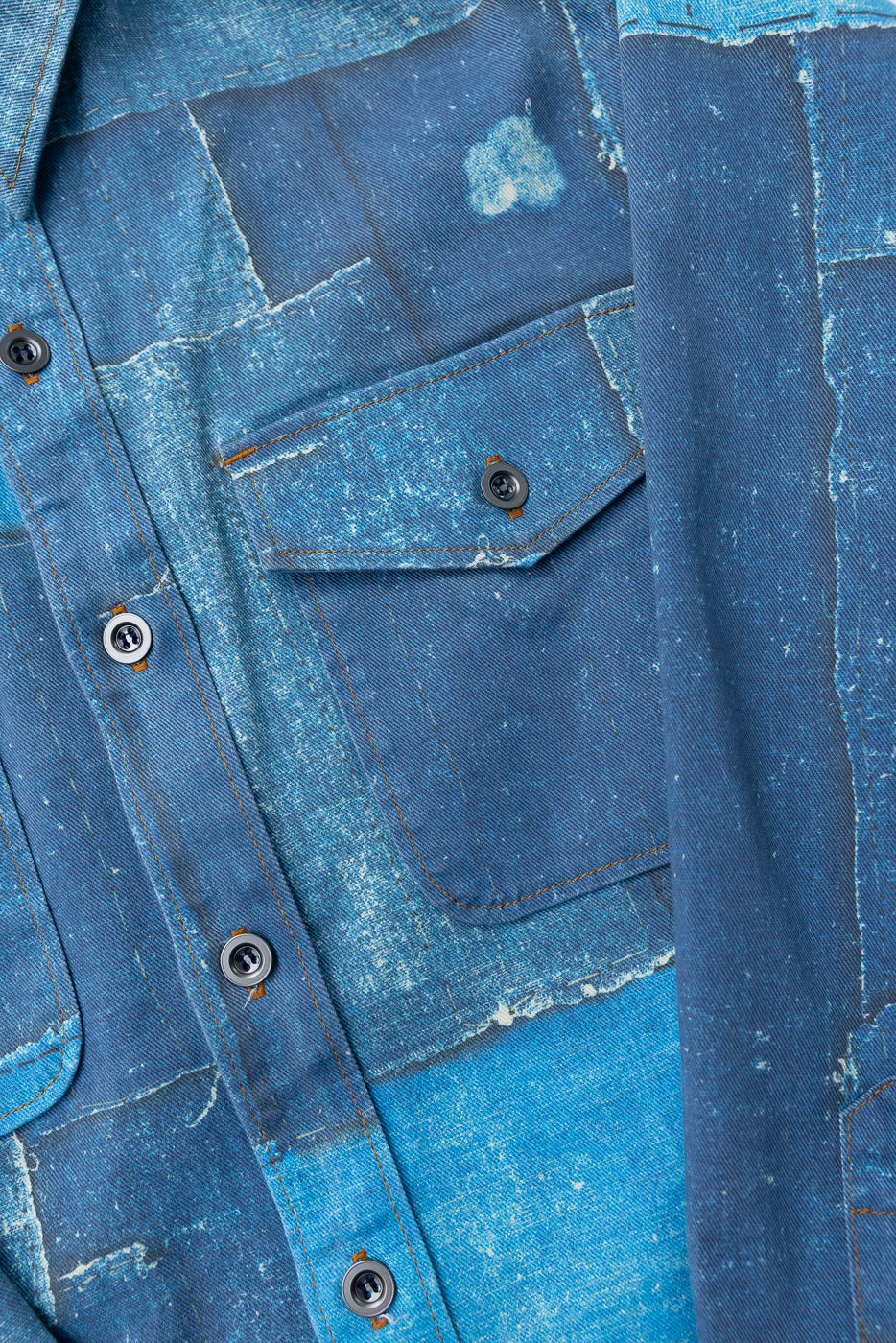 Close-up front view of distressed denim shirt with patchwork, contrast stitching, and buttoned chest pocket.