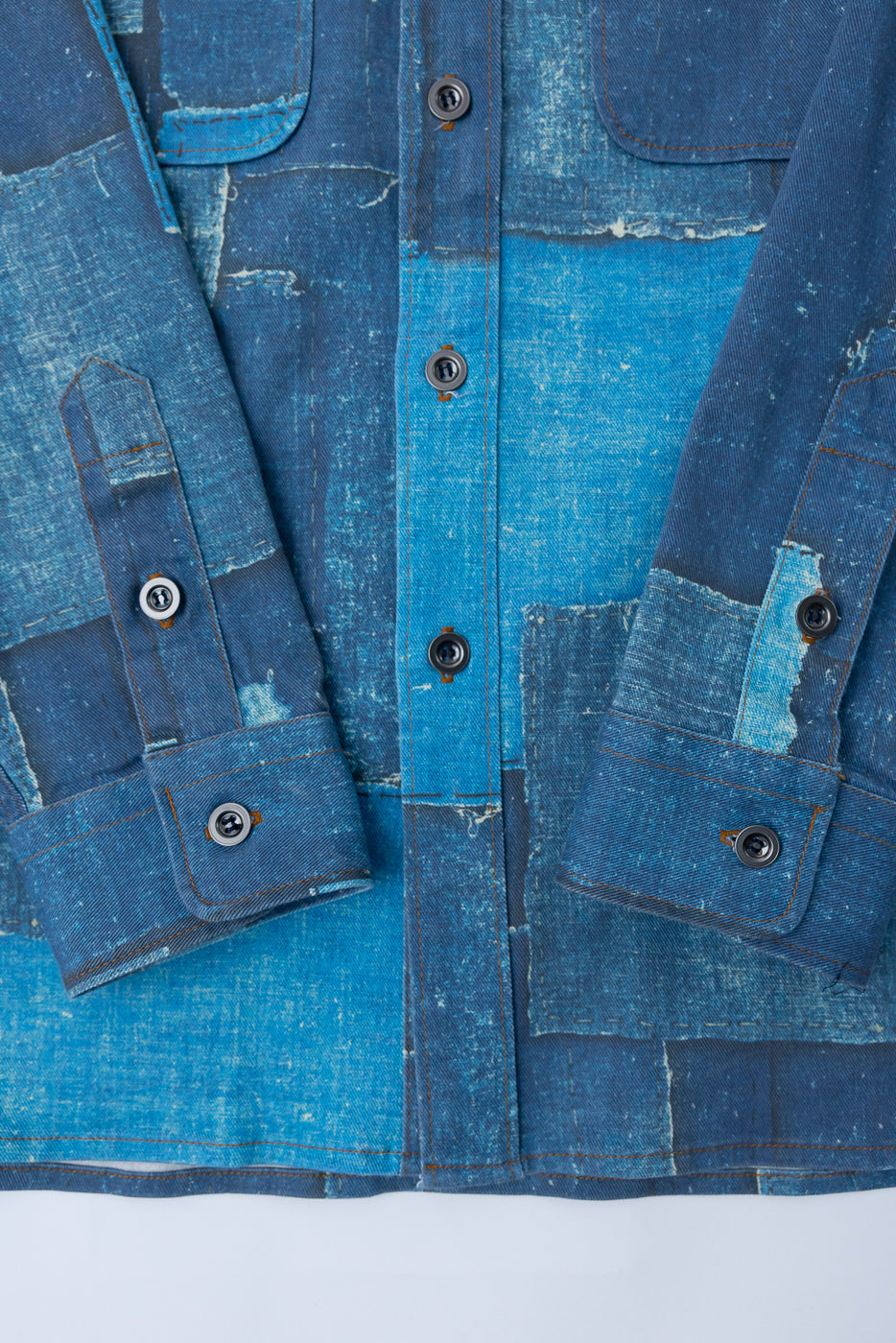 Close-up front view of patchwork denim shirt with button cuffs, selvedge details, and distressed texture