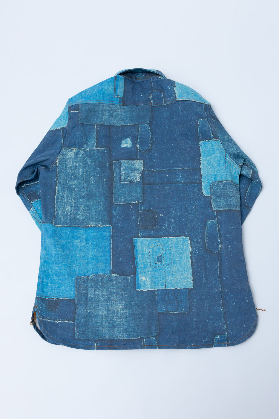 Back view flat lay of patchwork indigo denim shirt, showcasing varied blue tones and raw seam details