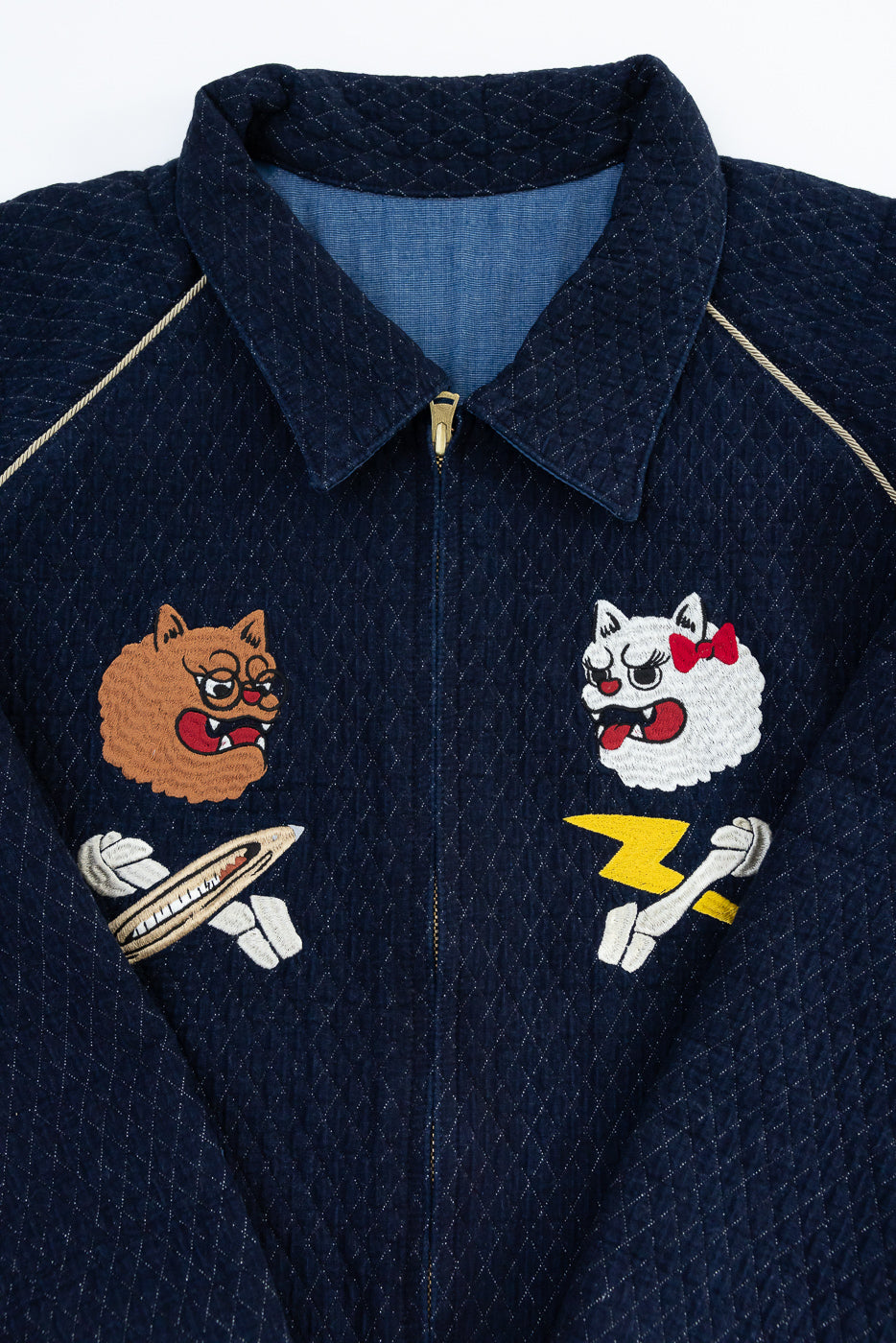 Close-up front of navy quilted jacket with cartoon cat embroidery, gold zipper, and diamond stitch detail
