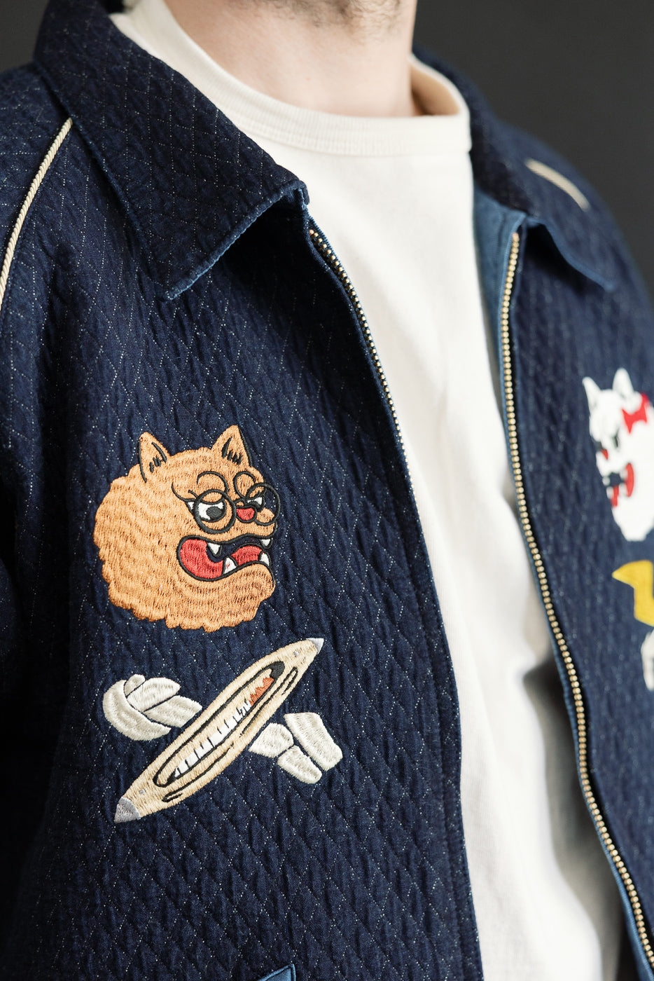 Close-up front view of navy quilted jacket with embroidered cat and rocket patches, worn by male model.