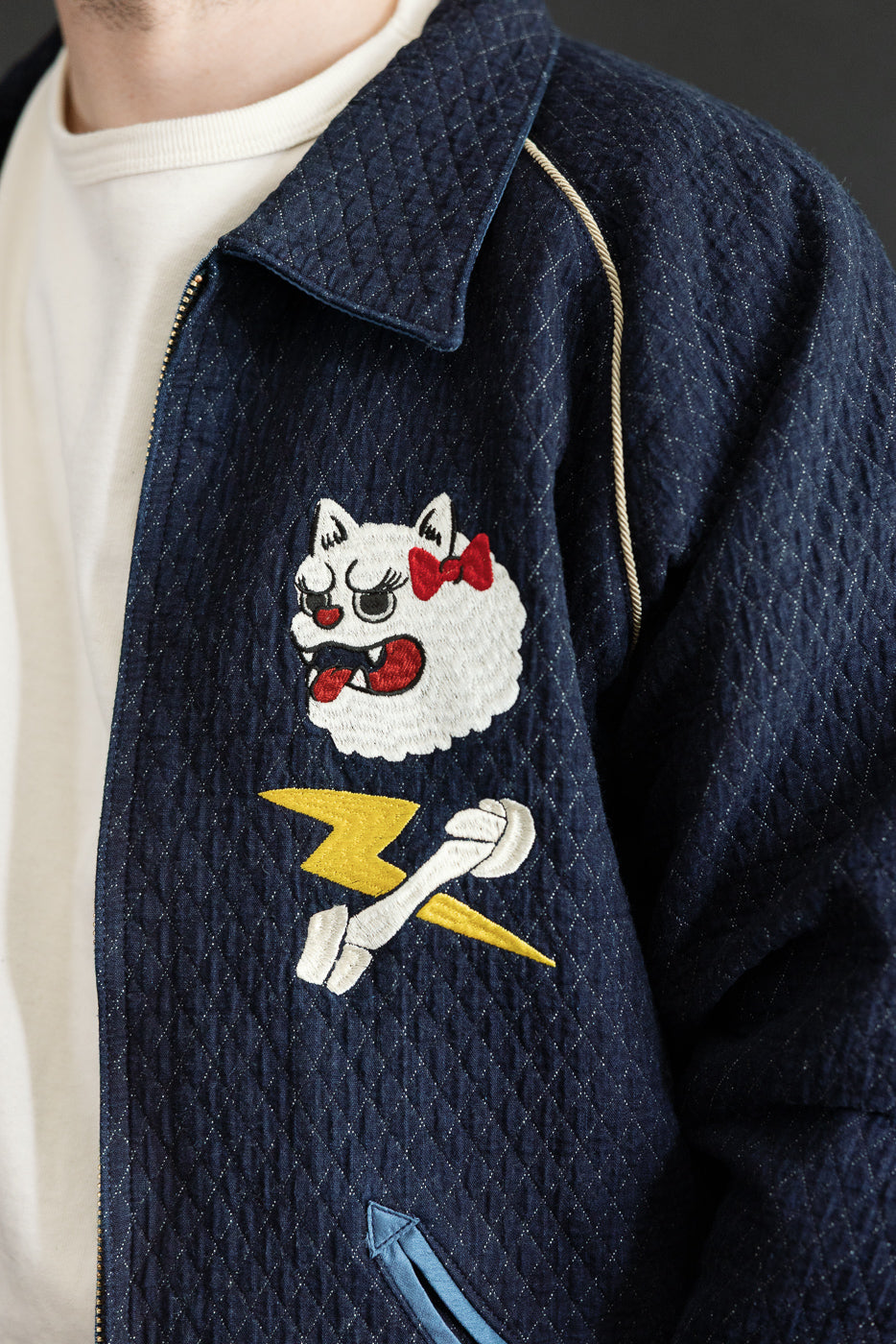 Close-up front view of navy quilted jacket with embroidered cat and lightning bolt, worn by male model.