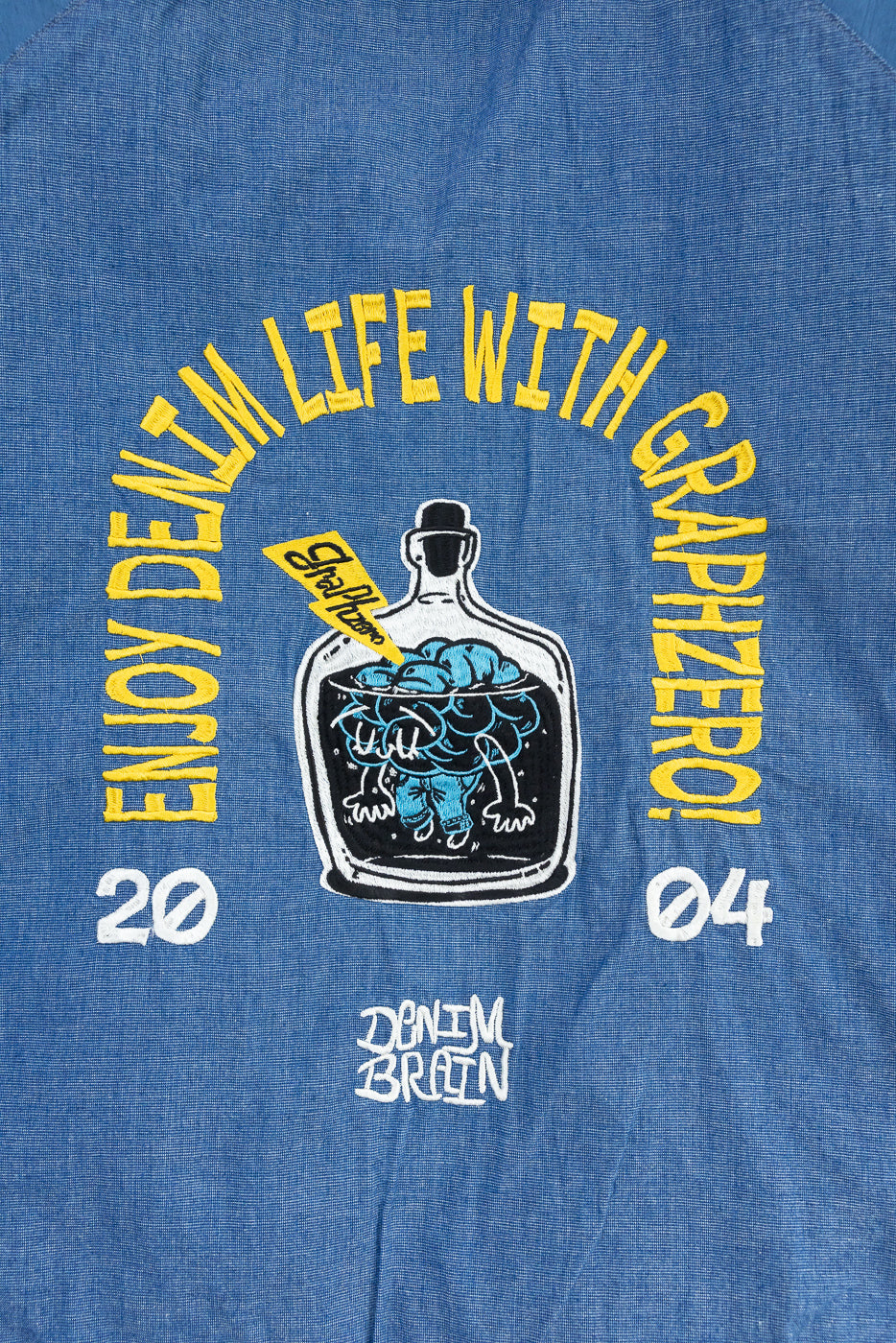 Close-up of blue denim shirt front with 'Enjoy Denim Life' graphic, bottle design, and 'Denim Brain' text.