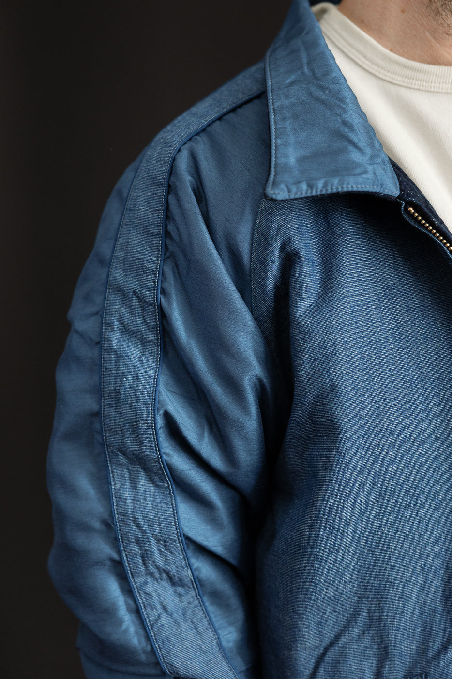 Close-up front-left view of men's blue denim jacket, showcasing collar, zipper, and fabric texture on athletic build model