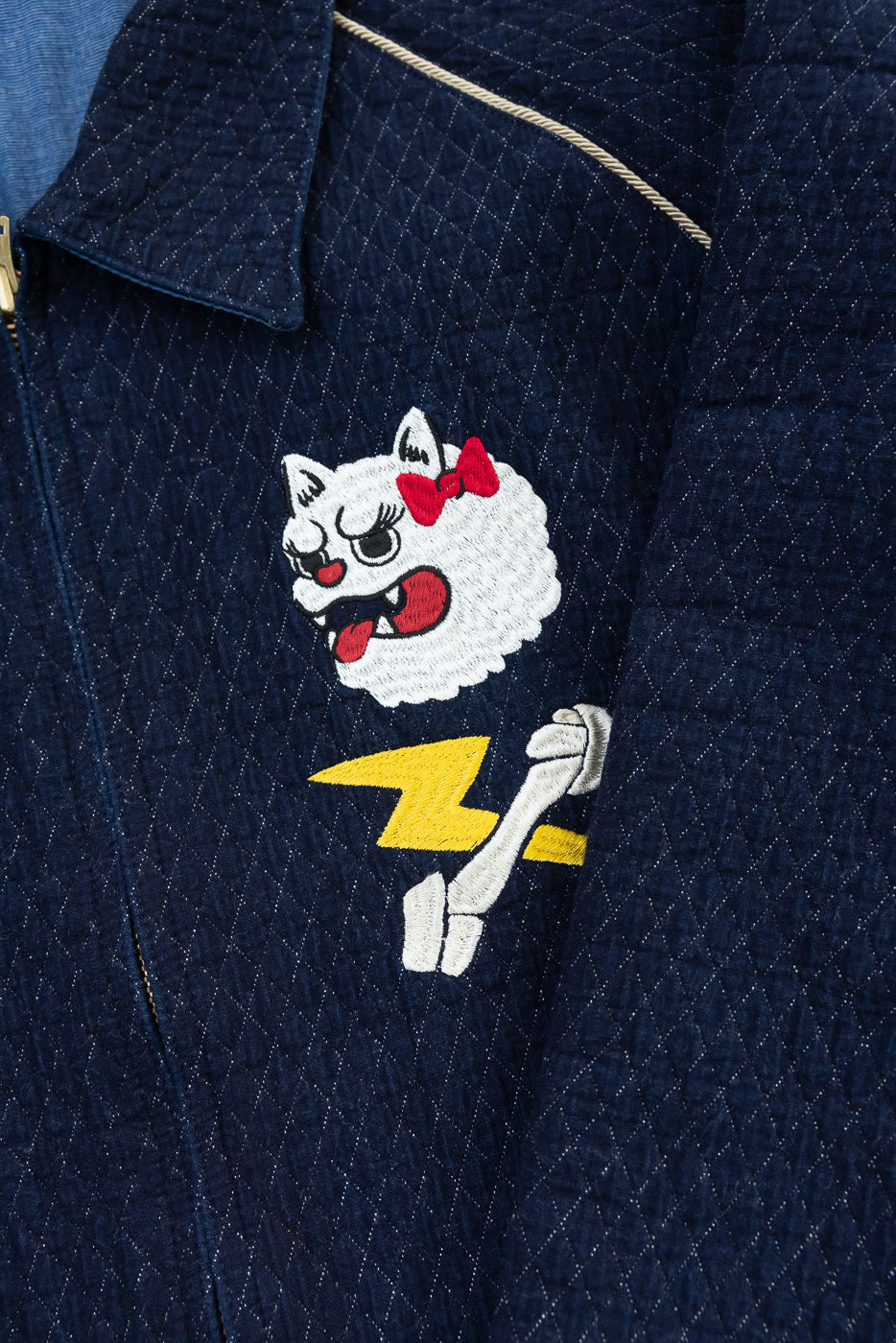 Close-up of navy quilted jacket front, featuring embroidered cat with red bow and yellow lightning bolt.