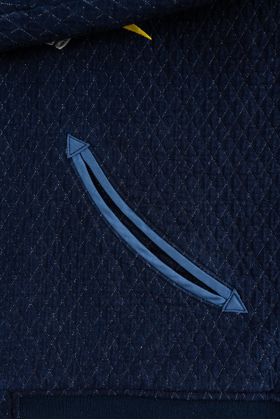 Close-up front view of navy quilted jacket with arrow-shaped zipper pocket, textured diamond stitching, and yellow tag detail