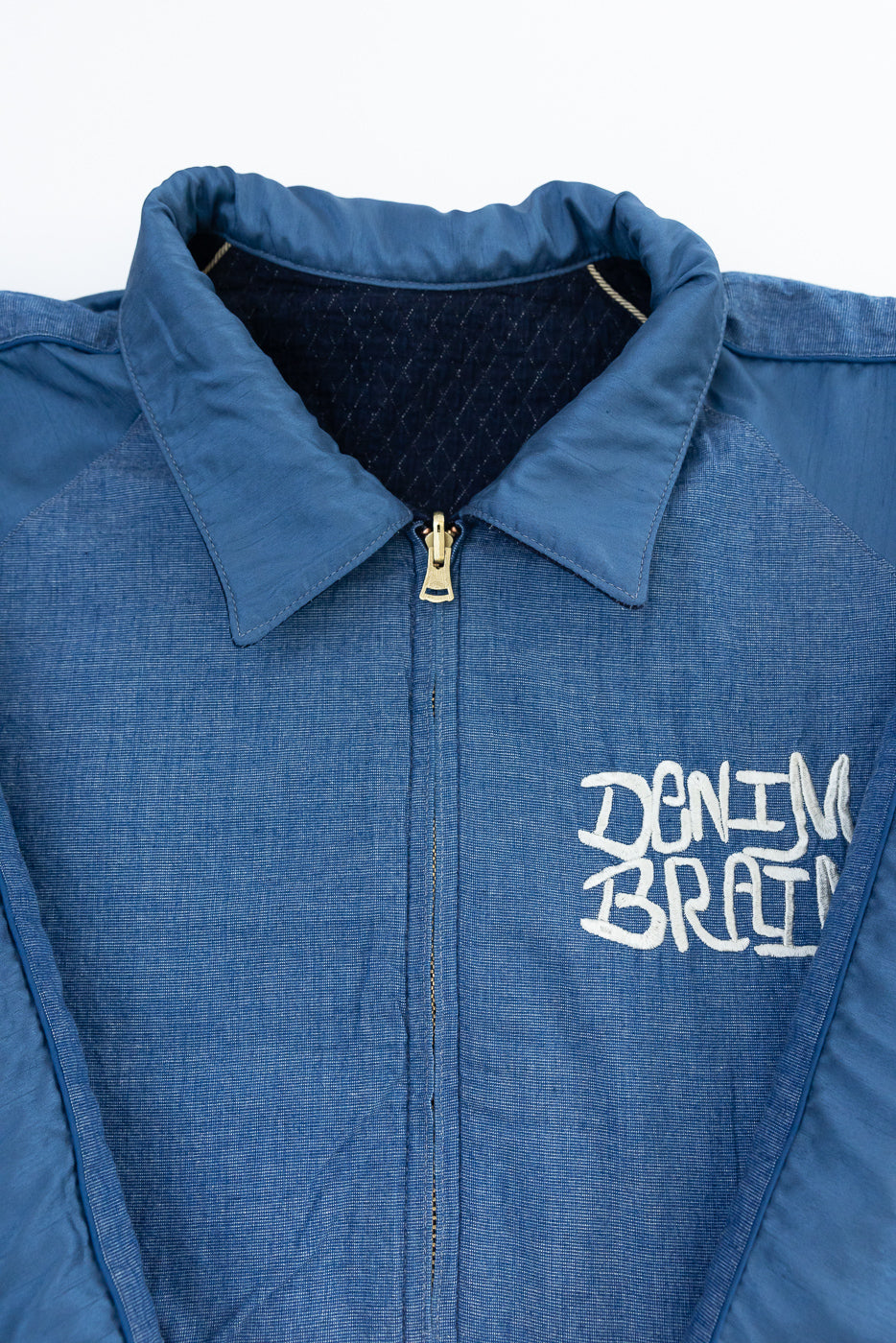 Close-up front view of blue denim jacket with 'DENIM BRAIN' embroidery, collar, and zipper details