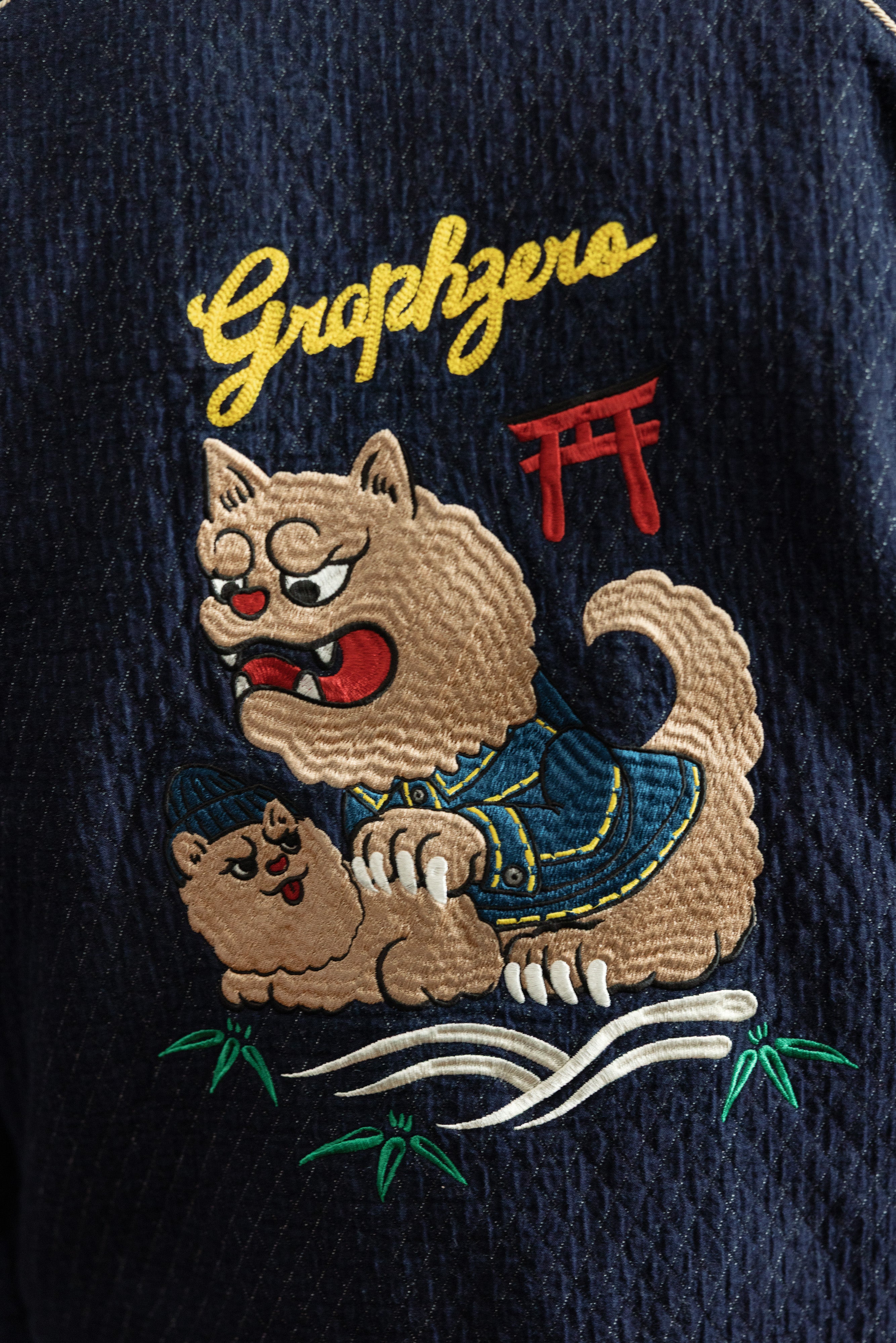 Close-up of embroidered cat design on dark denim jacket, front view, featuring 'Graphzero' text and detailed stitching.