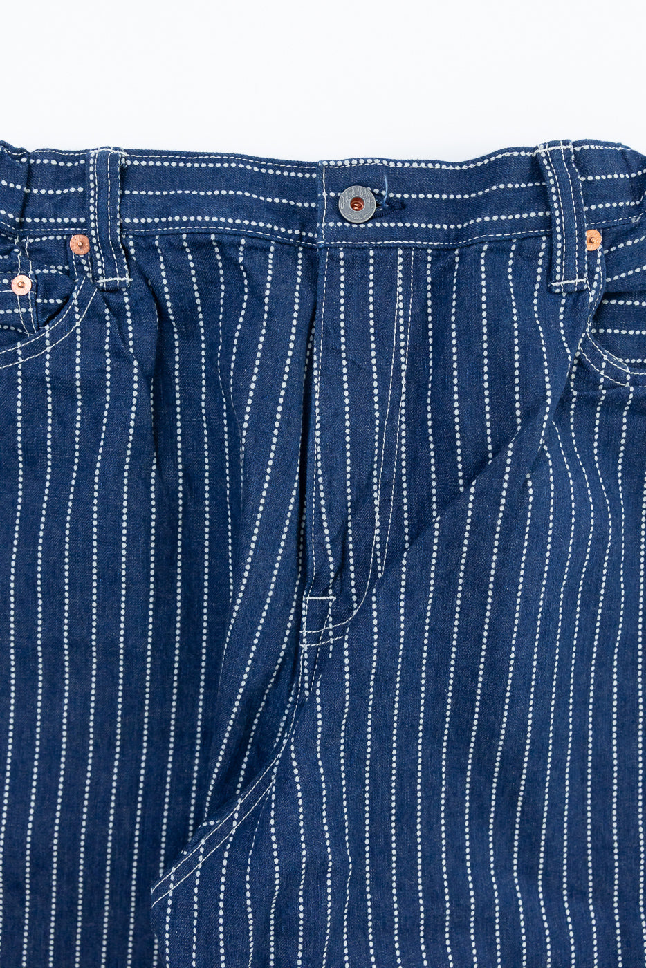 Close-up front view of indigo selvedge pants with white pinstripes, copper rivets, and button fly detail