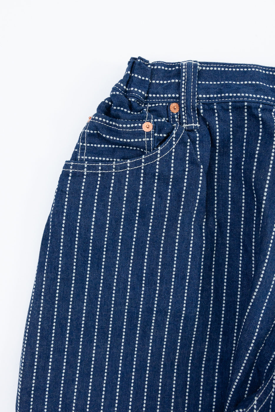 Close-up front view of striped denim pants with copper buttons and white stitching detail.