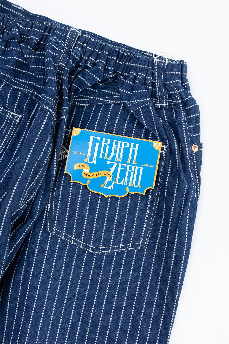 Close-up of back pocket with Graph Zero tag on striped denim pants, showcasing fabric texture and stitching.