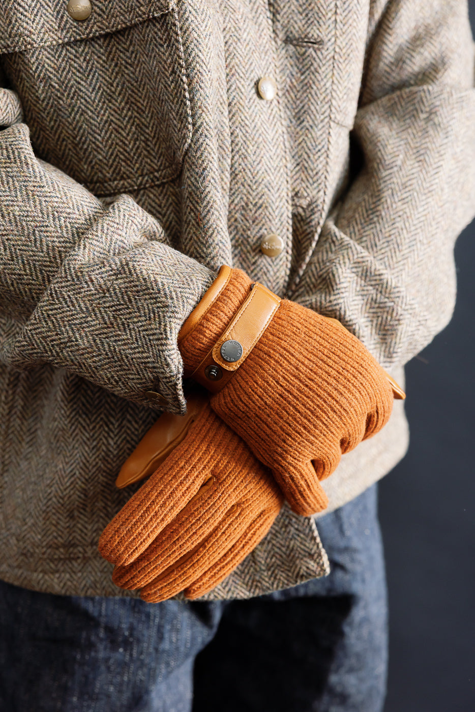 Close-up of Hestra Christopher cork knit gloves on male model, showing front glove detail and brown herringbone jacket from Dant.