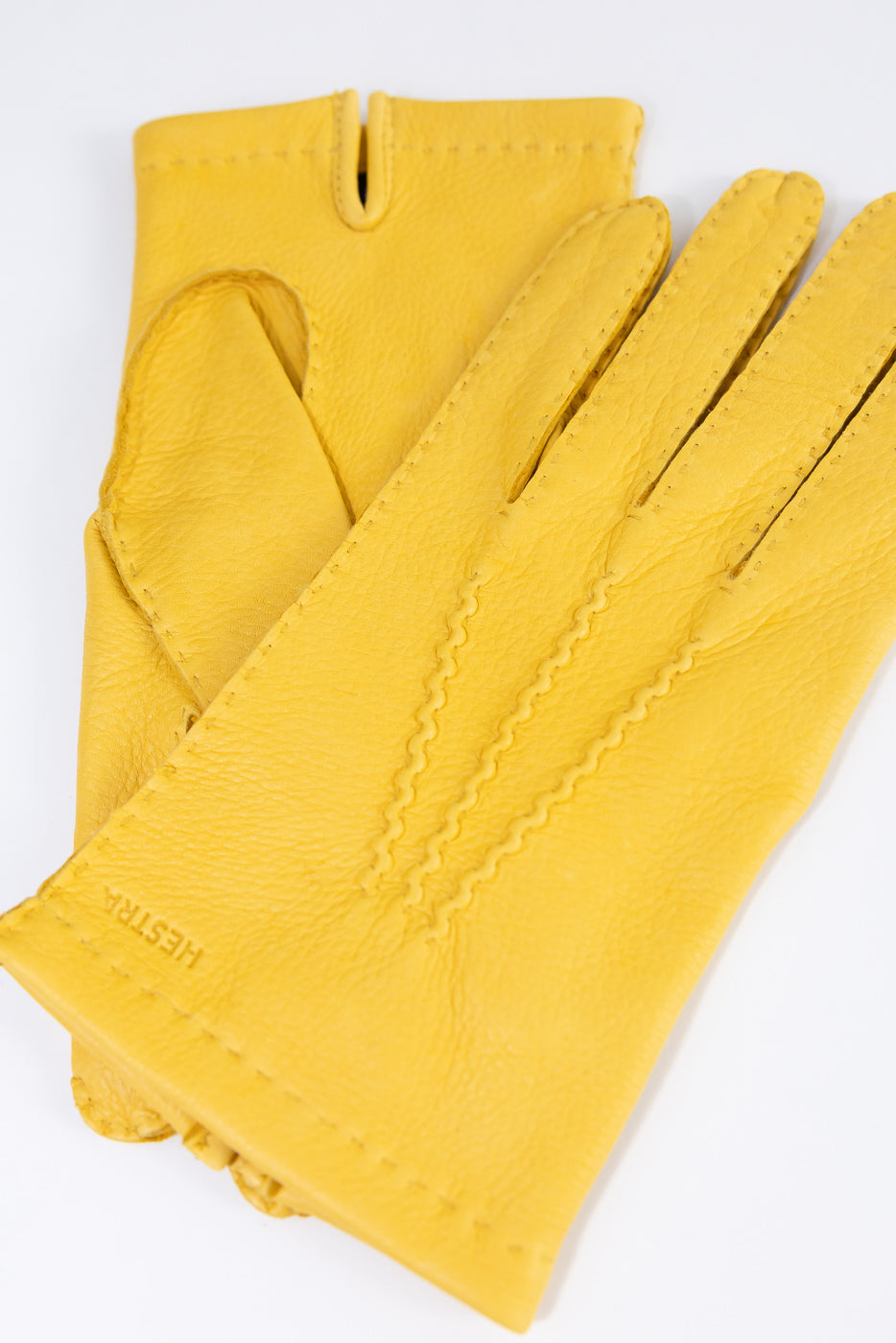 Close-up front flat lay of Hestra Henry yellow leather gloves, visible stitching detail