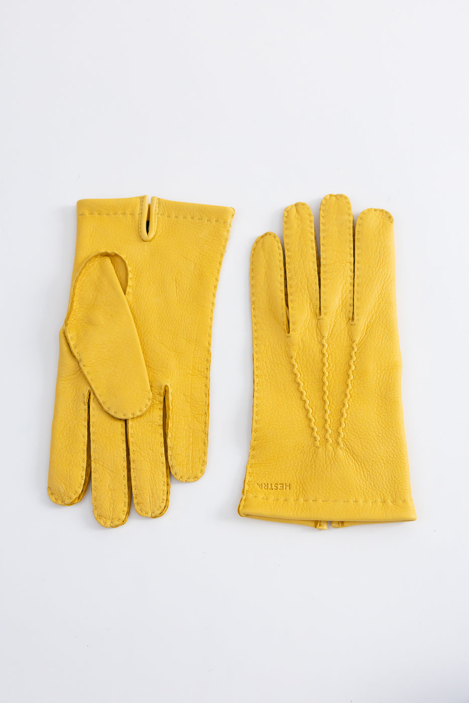 Flat lay of Hestra Henry natural yellow leather gloves, front and back details, visible stitching