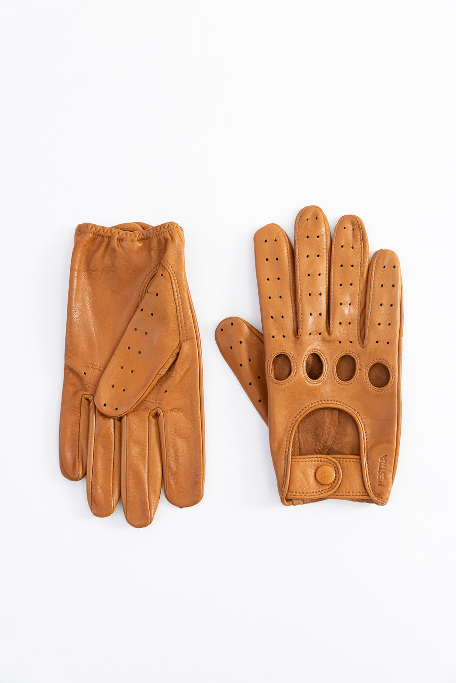 Flat lay of Hestra Morgan tan leather driving gloves, palm and back, perforated detailing, button closure.