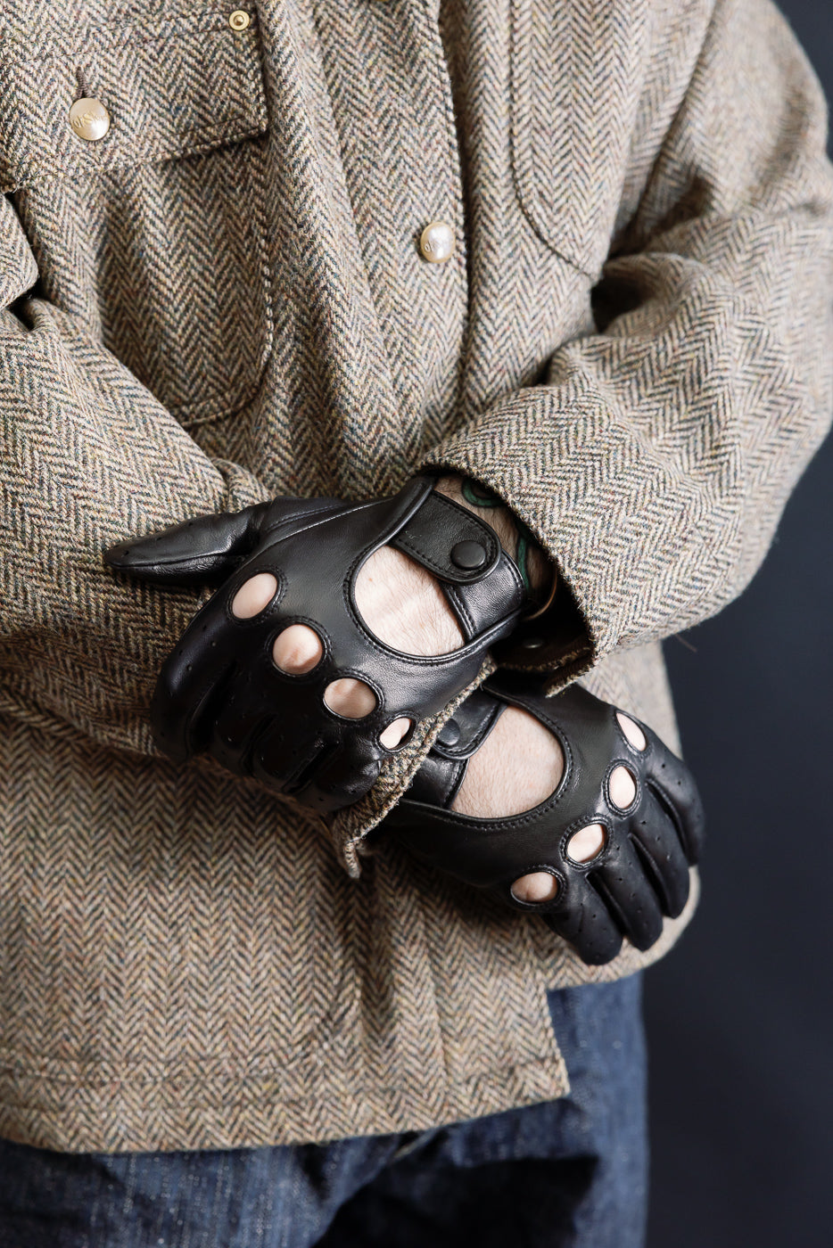 Close-up of men's black leather driving gloves with open knuckles, worn by male model 5'9