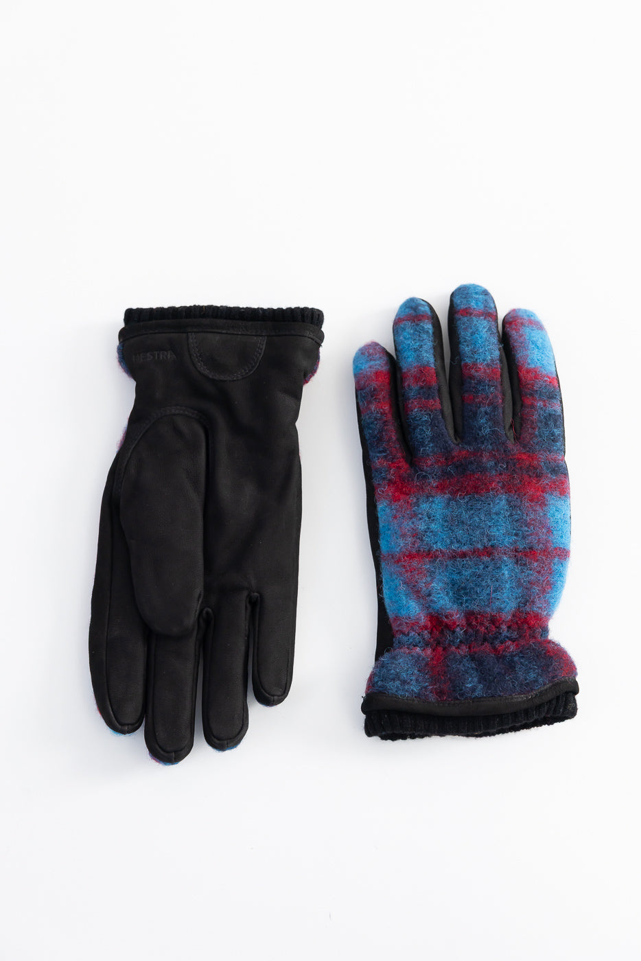 Flat lay of Hestra Noah gloves, one palm side in black suede, one back side in navy multi plaid wool, close-up.