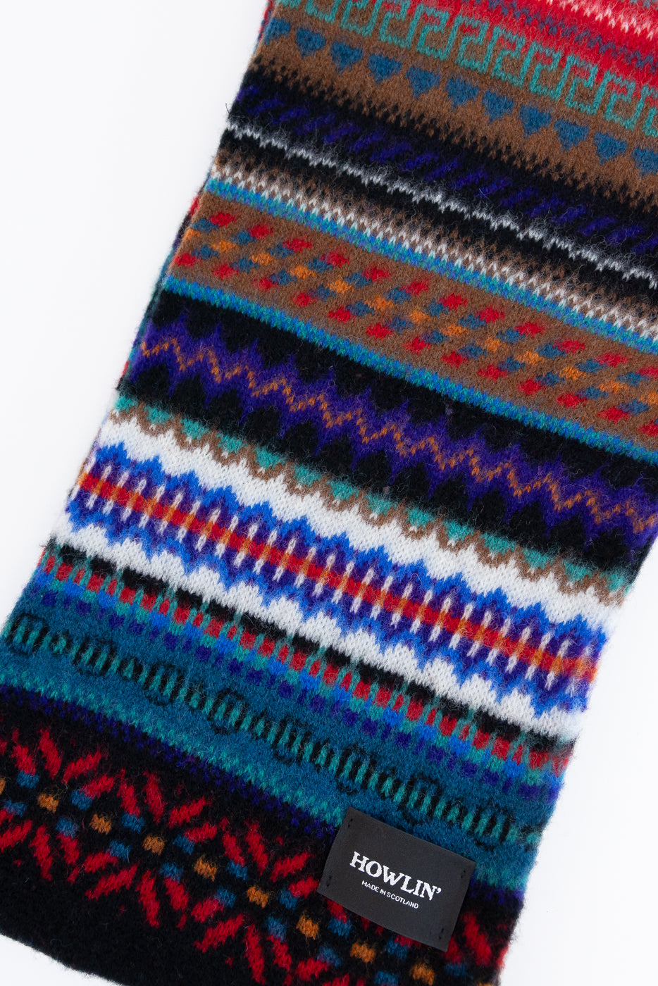 multicolored, patterned wool scarf with a black base on a white background, close up