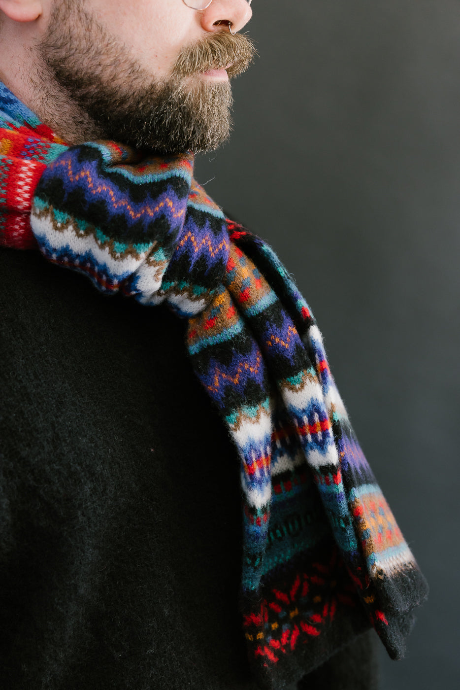 multicolored, patterned wool scarf with a black base on bearded man with a black sweater, close up