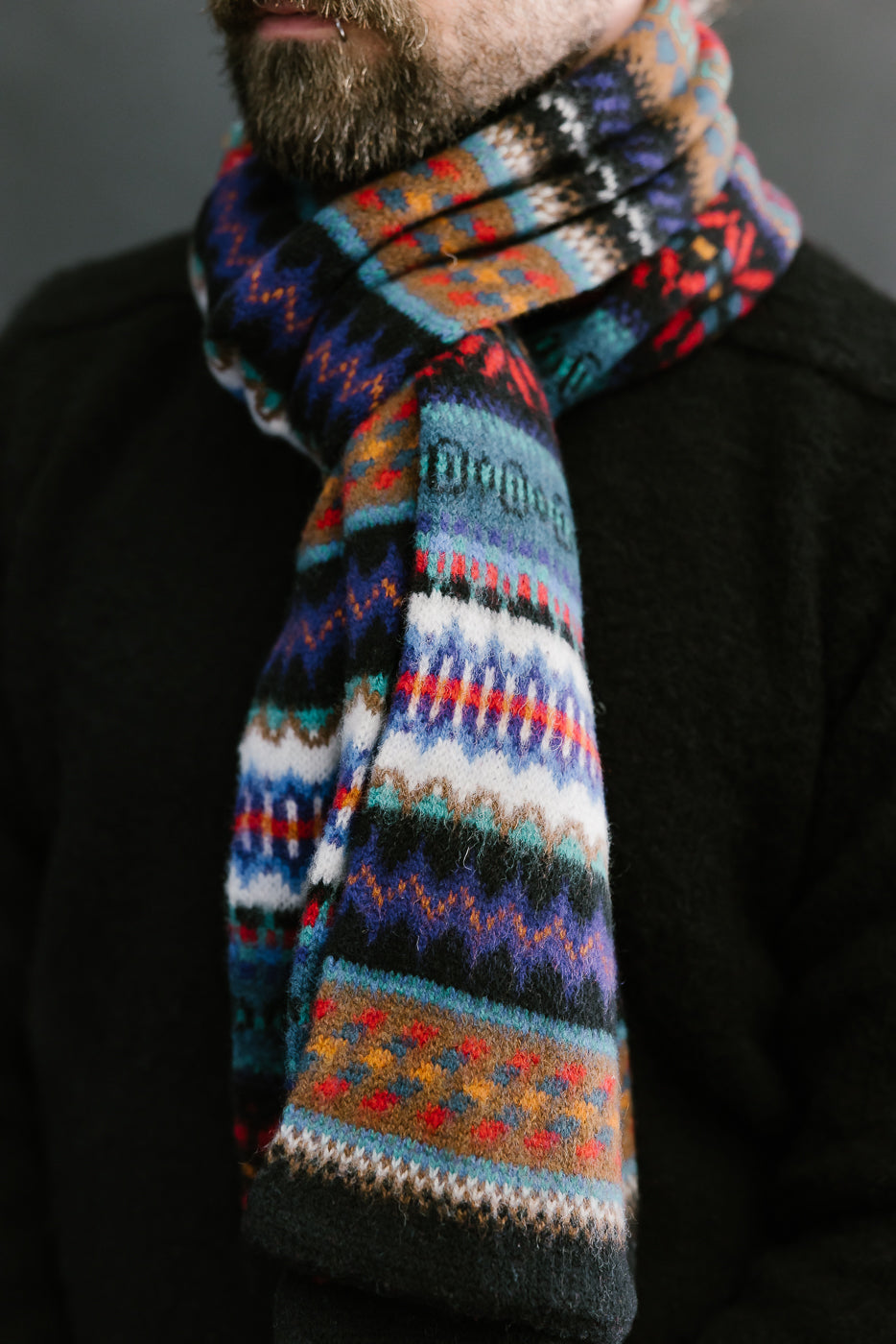multicolored, patterned wool scarf with a black base on bearded man with a black sweater, close up
