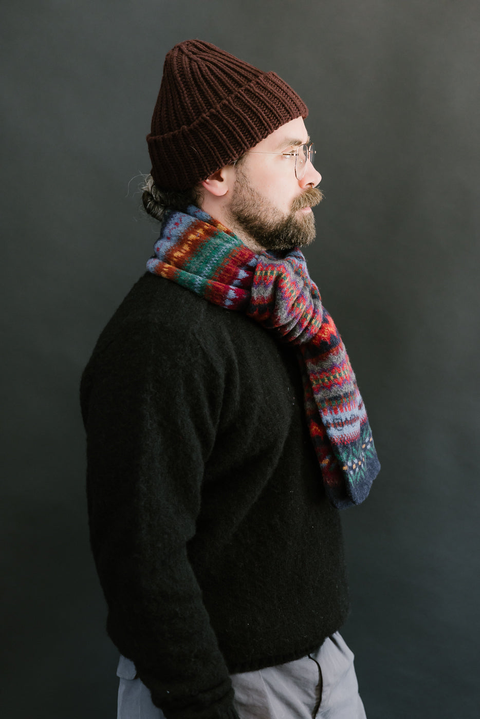 multicolored, patterned wool scarf with a navy base on a bearded man with a chocolate beanie, side view