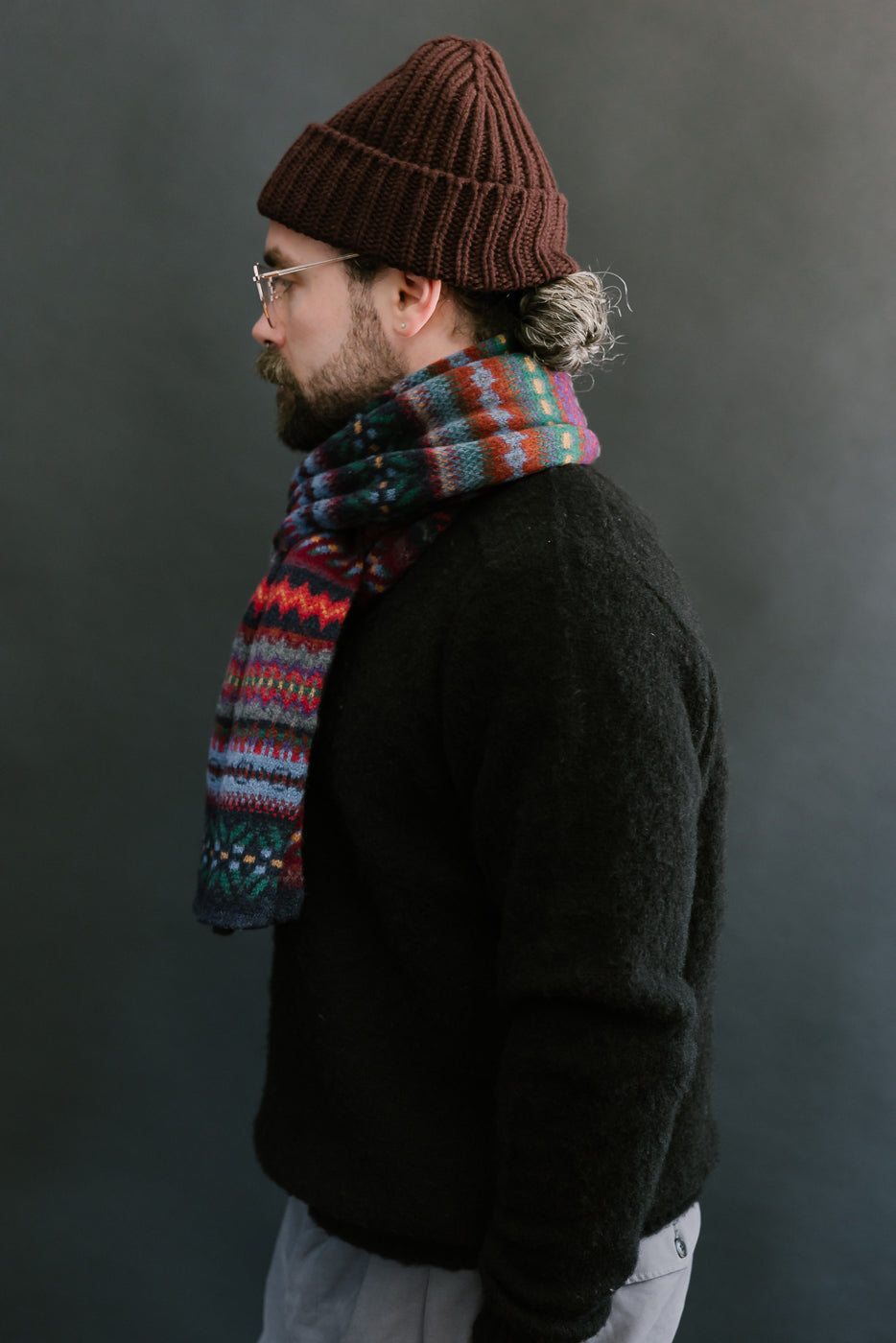 multicolored, patterned wool scarf with a navy base on a bearded man with a chocolate beanie, side view