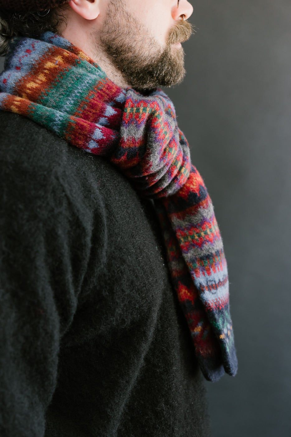 multicolored, patterned wool scarf with a navy base on a bearded man with a chocolate beanie, close up side view