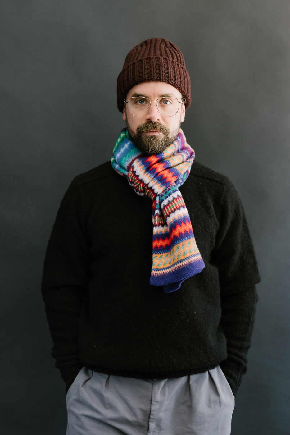 multicolored, patterned wool scarf with a purple base on a bearded man with a chocolate beanie and balck sweater, front view