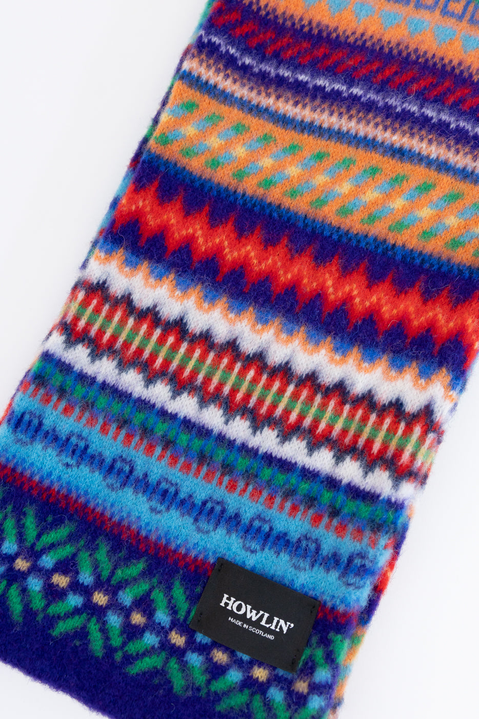 multicolored, patterned wool scarf with a purple base on a white background, close up