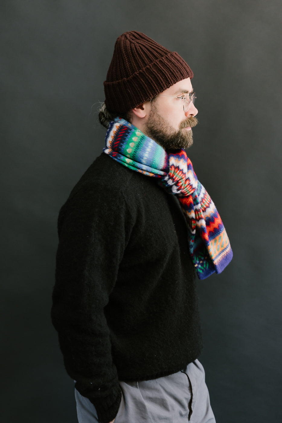 multicolored, patterned wool scarf with a purple base on a bearded man with a chocolate beanie and balck sweater, side view