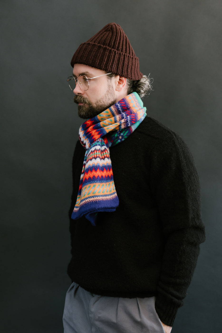 multicolored, patterned wool scarf with a purple base on a bearded man with a chocolate beanie and balck sweater, side view
