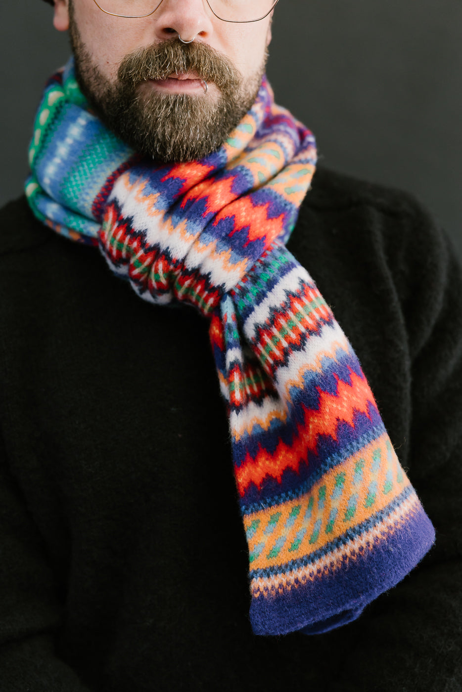 multicolored, patterned wool scarf with a purple base on a bearded man with a chocolate beanie and balck sweater, close up